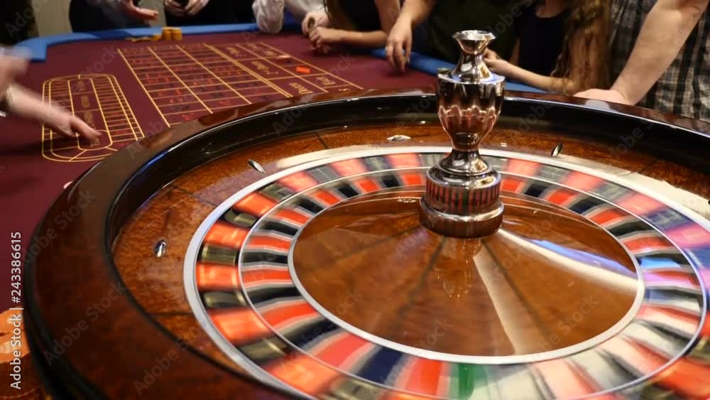 Closeup shot of casino roulette spinning around with casino chips put in piles near. Hands of urecognizable people holding cards and chips, people gambling. Casino concept. Dealer hand moves the Closeup shot of casino roulette spinning around with casino chips put in piles near. Hands of urecognizable people holding cards and chips, people gambling. Casino concept. Dealer hand moves the