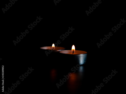 Two lighted candles with an orange flame and isolated on a black background