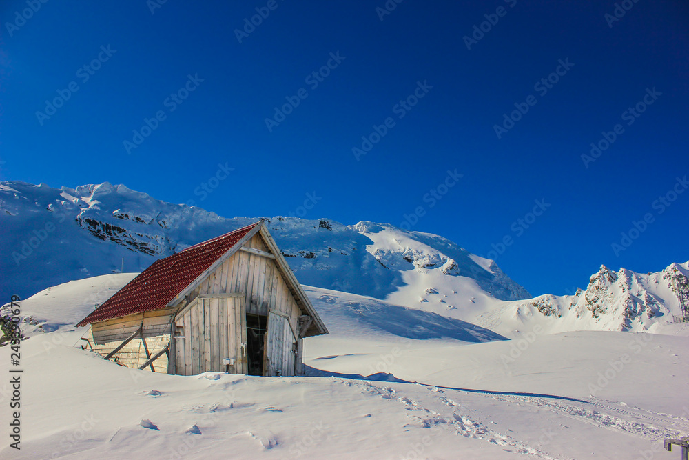 Winter landscape with wooden toolshed and Fagaras Mountains covered in thick layer of snow at Balea lake, Sibiu county, Romania