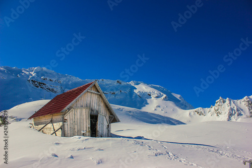 Winter landscape with wooden toolshed and Fagaras Mountains covered in thick layer of snow at Balea lake, Sibiu county, Romania