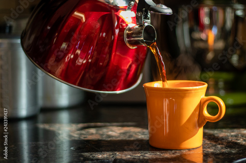 Pouring tea into orange mug on counter