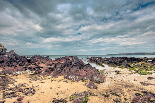 Rocky beach and moody sky over sea horizon on Pembrokeshire coast,Uk.Red rock formation on diverse shoreline.Nature image with copy space. © Jazzlove