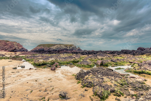 Scenic landscape with moody sky over Pembrokeshire coast  Uk.Rocky beach with sand and puddles of sea water during low tide.