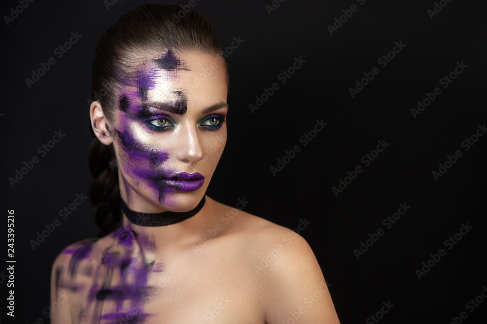 A portrait of a young, self-confident, daring and seductive girl. She is posing in a dark background demonstrating her character, image, makeup and the colorful highlights of the light on her face.