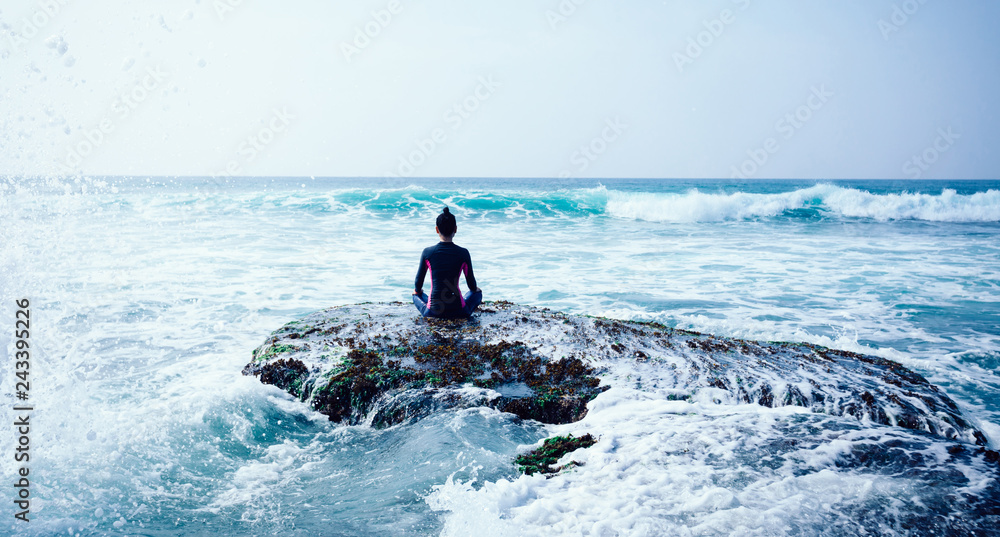 Woman meditation at the seaside croal cliff edge facing the coming strong sea waves - obrazy, fototapety, plakaty 