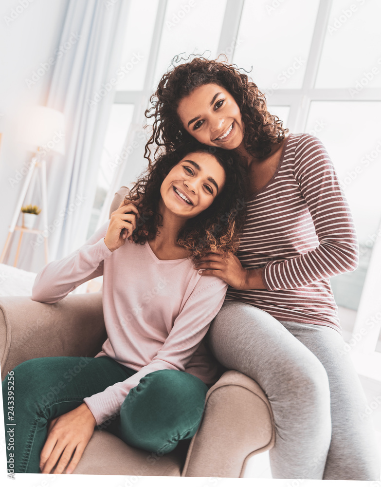 Smiling sister in grey leggings sitting near her older sister Smiling sister in grey leggings sitting near her older sister