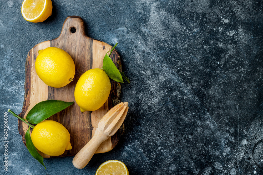 Fresh ripe lemons with leaves on wooden board with  reamer over black stone background. Top view, copy space