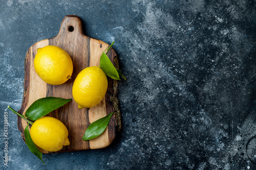 Fresh ripe lemons with leaves on wooden board over black stone background. Top view, copy space