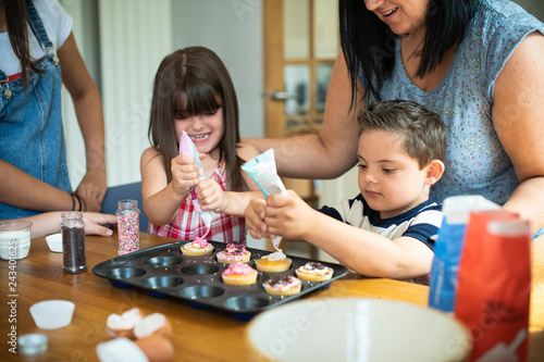 Mother helping son to put frosting onto cupcakes