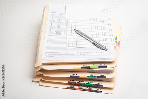 A stack of color-coded and numbered patient medical records with blank doctor's office visit form, ledger card, and ballpoint pen.