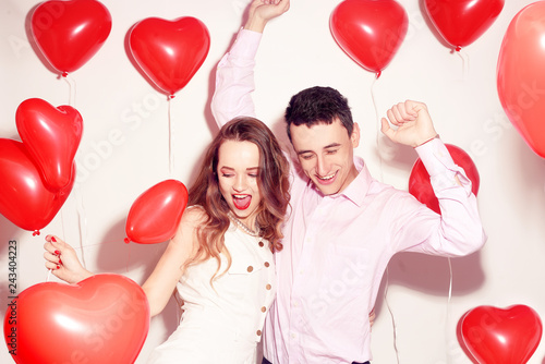 Man with his lovely sweetheart girl dance and have fun at Lover's valentine day. Valentine Couple. Couple very happy, party time, smile, laugh. Background red balloons hearts. Love concept. Crazy.