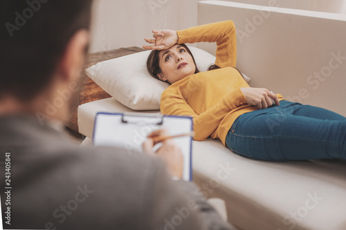 Beautiful stressed woman feeling anxious lying on sofa near therapist