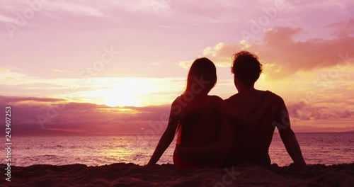 Couple sitting romantic at beach sunset in love at honeymoon vacation travel
