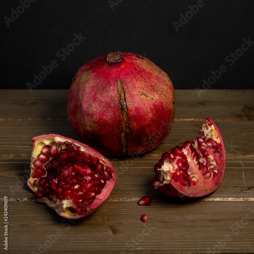 Two pomegranate fruits on wooden table one whole and one cut photo