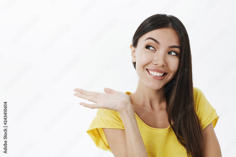 Girl showing product changed her life. Portrait of joyful pleased cute european female with dark hair in trendy yellow t-shirt stooping pointing left with arm near shoulder and smiling satisfied Girl showing product changed her life. Portrait of joyful pleased cute european female with dark hair in trendy yellow t-shirt stooping pointing left with arm near shoulder and smiling satisfied