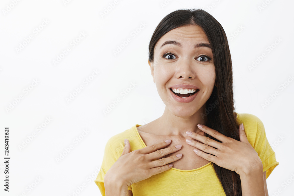 Surprised delighted attractive woman with lond dark hair holding palms on chest gasping and smiling from grateful feelings gazing with admiration and joy at camera, posing amazed over grey wall Surprised delighted attractive woman with lond dark hair holding palms on chest gasping and smiling from grateful feelings gazing with admiration and joy at camera, posing amazed over grey wall