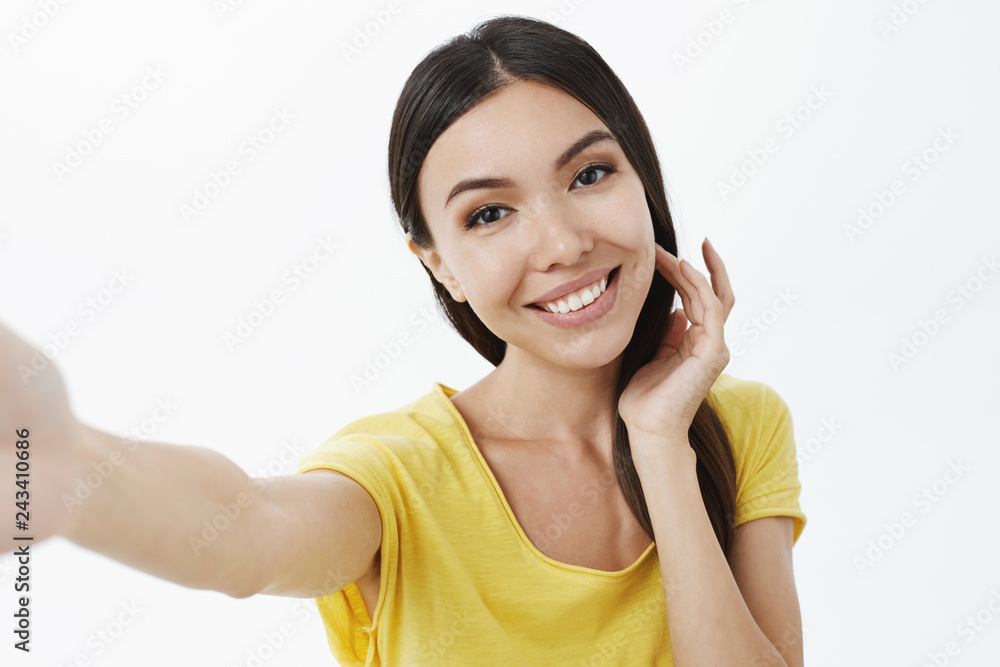 Making cute photo to send lover. Charming attractive and tender girl flicking hair strand flirty tilting head, smiling kind and gentle pulling hand forward taking selfie on smartphone over grey wall Making cute photo to send lover. Charming attractive and tender girl flicking hair strand flirty tilting head, smiling kind and gentle pulling hand forward taking selfie on smartphone over grey wall