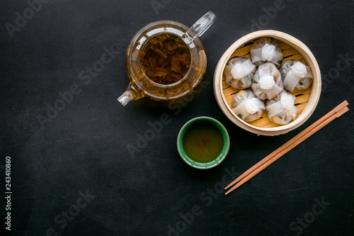 Chinese steamed dumplings Dim Sum in bamboo steamer with tea on black background top view mock up © 9dreamstudio