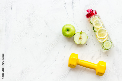 Healthy fruit water for sport, fitness. Bottle of water with lemon and cucumber near sport equipment dumbbells on white stone background top view copy space