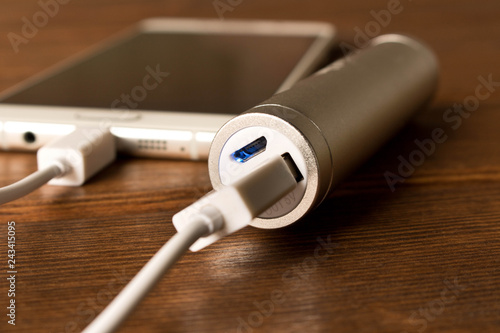 Silver power bank charging smartphone on wooden table