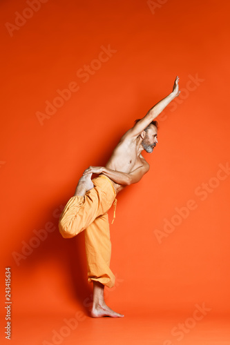Fotobehang Old man practicing yoga doing stretching exercises against orange background