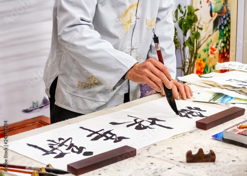 Asian caligraphy. The master of Chinese Caligraphy writes on rice paper characters and hieroglyphs that read Xin nian kuai le and are translated as Happy New Year.