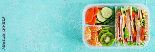 School lunch box with sandwich, vegetables, water, and fruits on table. Healthy eating habits concept. Flat lay. Banner. Top view