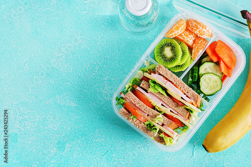 School lunch box with sandwich, vegetables, water, and fruits on table. Healthy eating habits concept. Flat lay. Top view