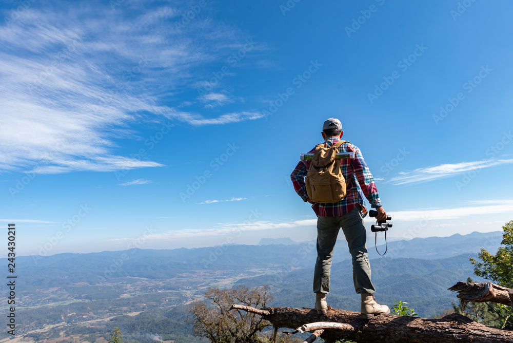 Young man with backpack and holding a binoculars standing on top of mountain. successful people concept