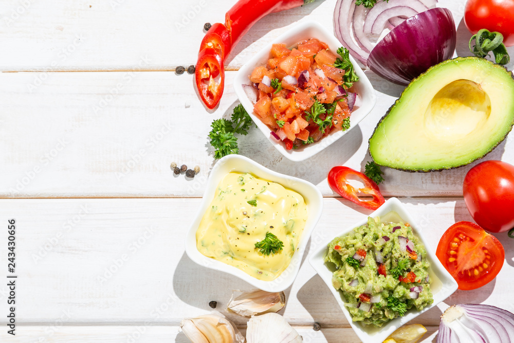 Selection of mexican sauces - salsa, guacamole, cheese sauce and ingredients, white wood background Selection of mexican sauces - salsa, guacamole, cheese sauce and ingredients, white wood background