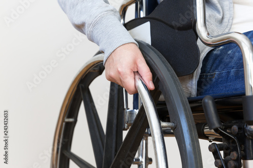Detail of disabled woman holding a hand on wheel of a wheelchair.