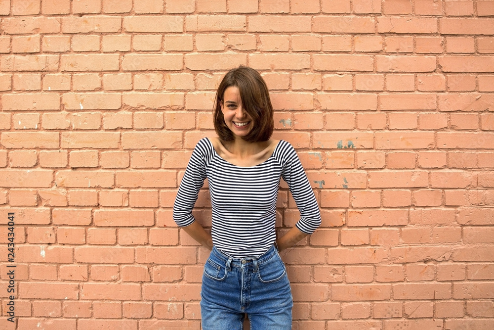 The girl is happy and smiling against the brick wall. Copy space, close up.