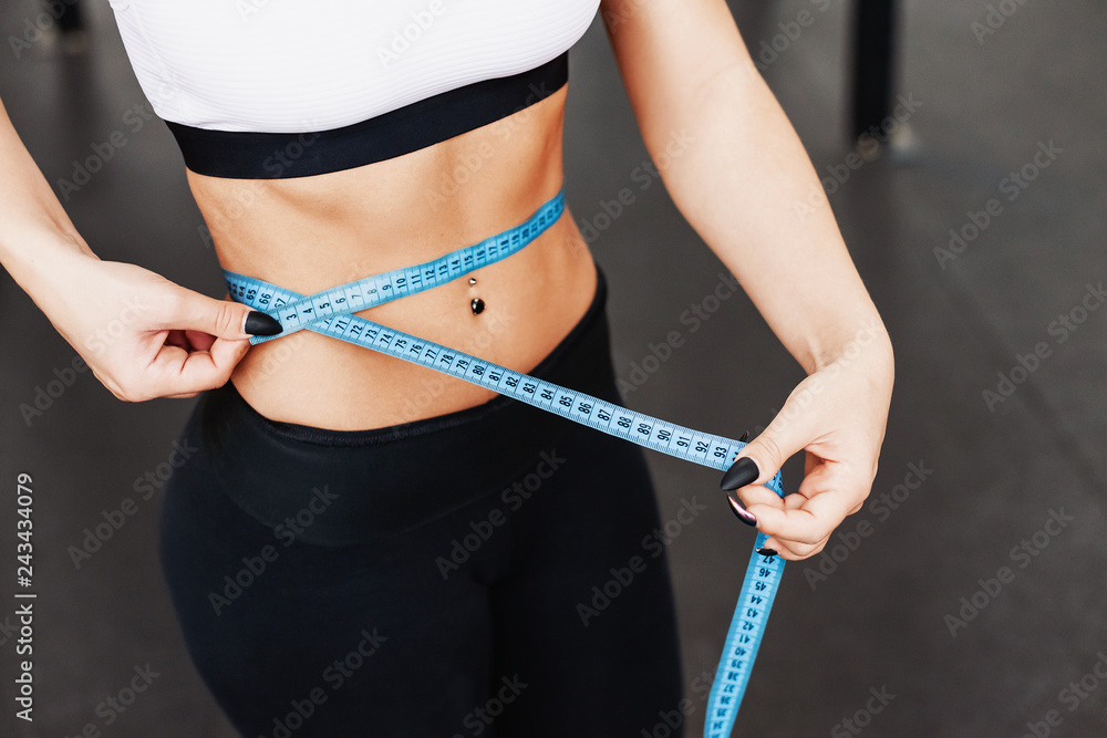 Photo of Young slim woman measuring her waist with a tape