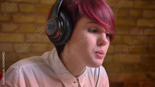 Close-up portrait of young short-haired female streamer in headphones gets extremely happy on bricken wall background. photo