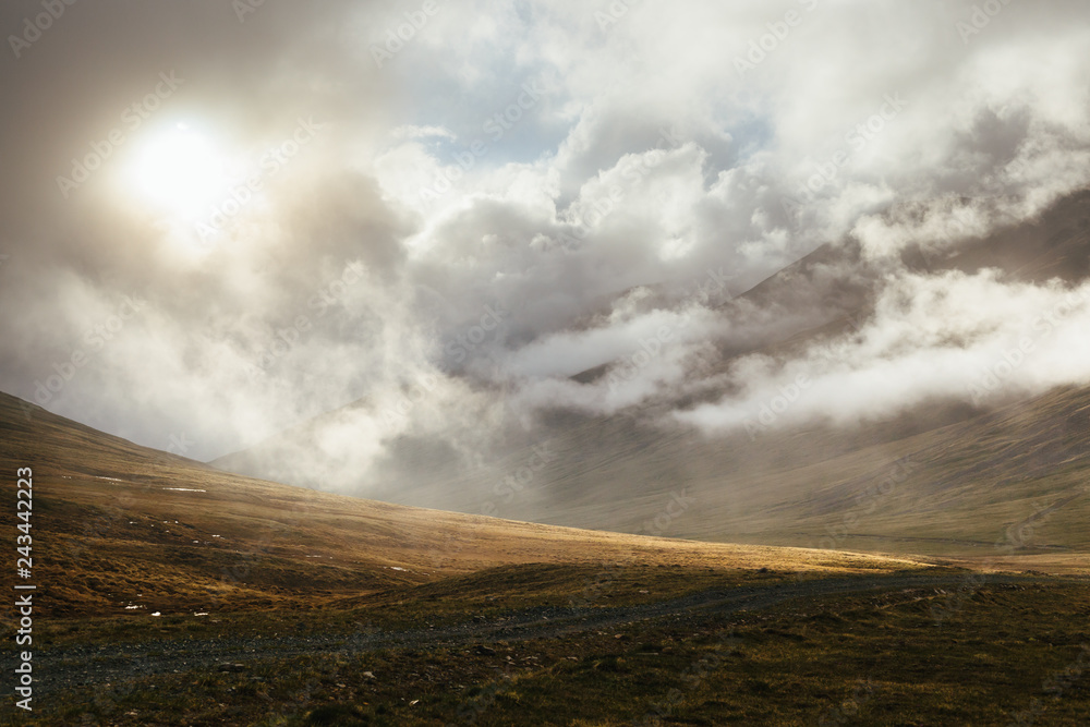 Dramatic sunlight through the low clouds on a mountain pass. Weather getting clear after the storm in the mountains. Fantastic cloudy background