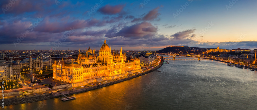 Obraz premium Budapest, Hungary - Aerial panoramic view of the beautiful illuminated Parliament of Hungary with Szechenyi Chain Bridge, Buda Castle Royal Palace and colurful clouds at background at sunset