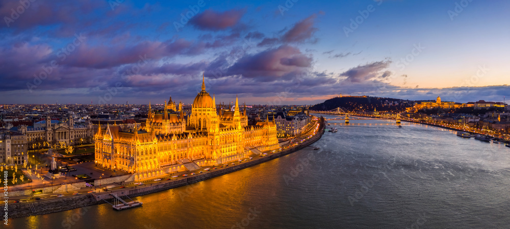 Fototapeta premium Budapeszt, Węgry - Widok z lotu ptaka na piękny oświetlony Parlament Węgier z mostem łańcuchowym Szechenyi, Pałac Królewski w Budzie i kolorowe chmury na tle o zachodzie słońca