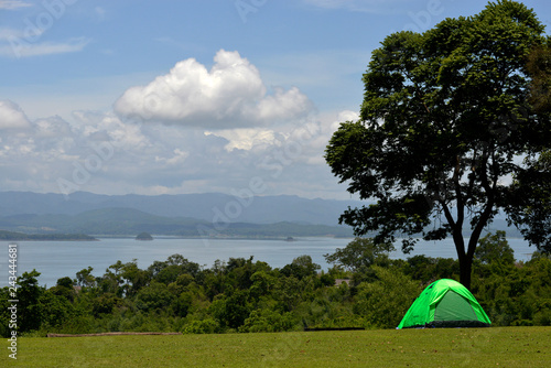 Green tent in a grass field with lake and blue sky in background