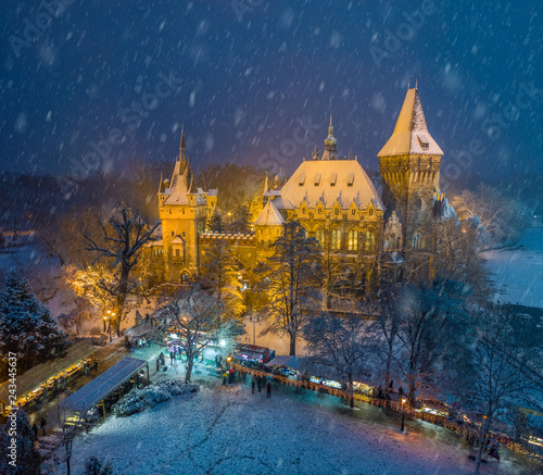 Budapest, Hungary - Christmas market in snowy City Park (Varosliget) from above at night with snowy trees and Vajdahunyad castle