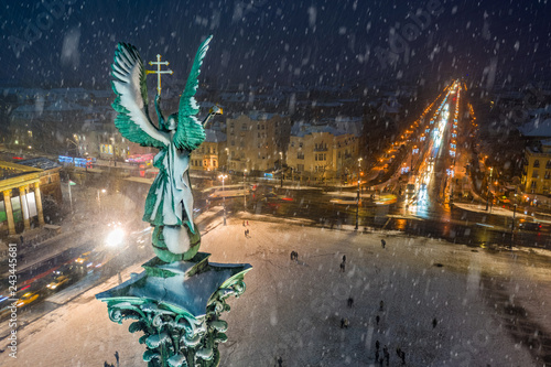 Budapest, Hungary - Aerial view of angel sculpture at Heroes' Square (Hosok tere) with Christmas decorated Andrassy street and trolley bus. Heavy snowing in Budapest © zgphotography