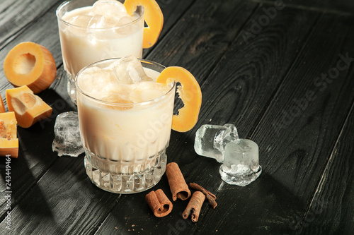 Close up view on white proteinaceous egg, alcohol cocktail in glasses. Glass with ice, pumpkin and cinnamon standing on dark wooden background. Copy free space for your text, logo or brand. photo