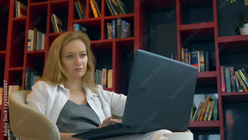 Young woman smiling. uses a laptop while sitting in a modern library. Young woman smiling. uses a laptop while sitting in a modern library.
