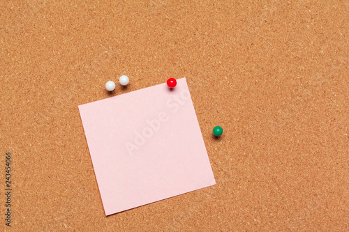 Sticky note pinned on cork board with thumbtacks