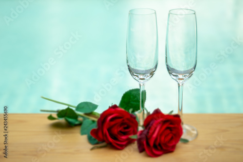 Two empty champagne glasses with rose flower next swimming pool.