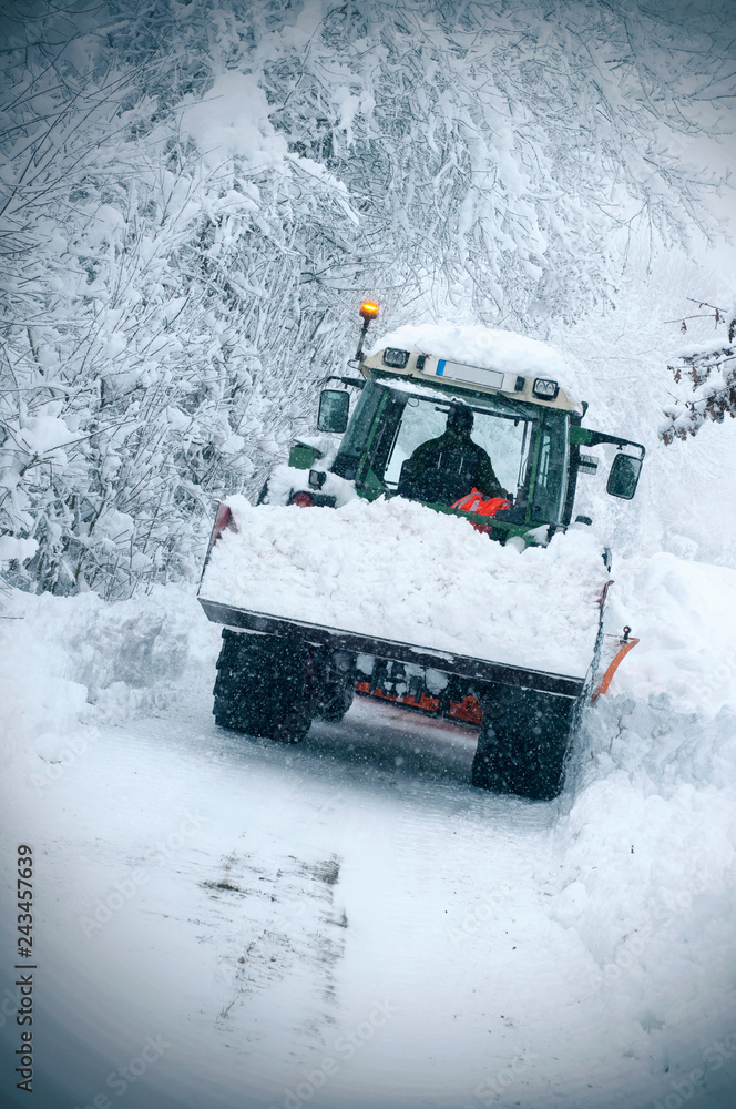 Winter service tractor cleaning the road surface to prevent icing in stormy snow winter day. Countryside view of a tractor cleaning the road in village Winter service tractor cleaning the road surface to prevent icing in stormy snow winter day. Countryside view of a tractor cleaning the road in village