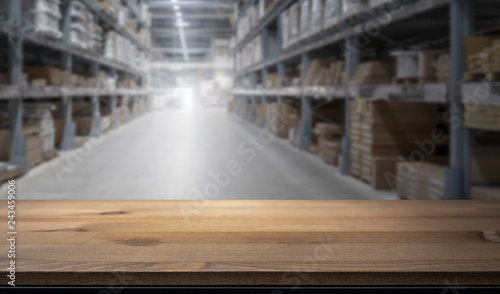 Wooden table top for product display montage. Blured shelves with goods in store at factory warehouse storage in the background. Stock concept.