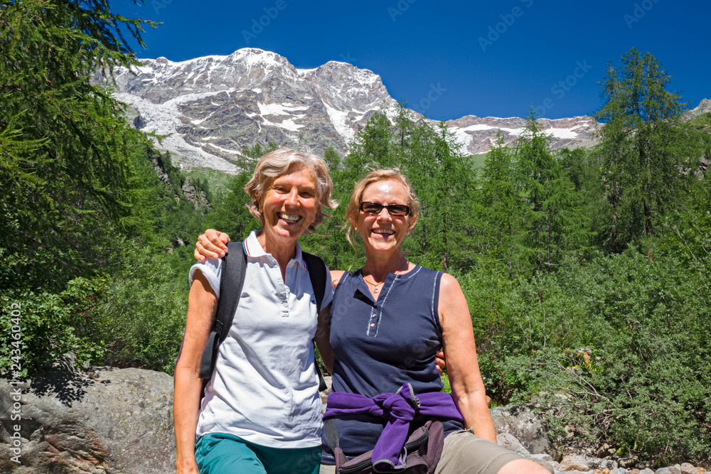 Naklejka premium Two hiker friends greet in a break during a climb on the paths on the slopes of Mount Rosa in Piedmont, Italy.