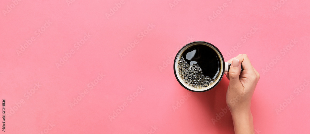 Minimalistic style woman hand holding a cup of coffee on pink background. Flat lay, Top view banner with copy space for you design
