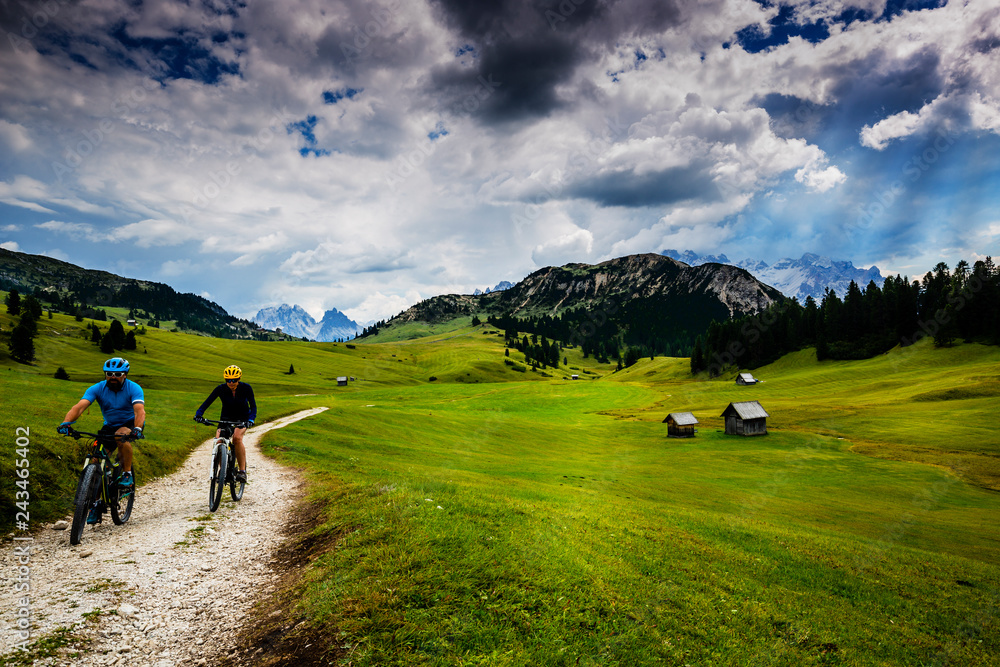 Couple cycling in Cortina d'Ampezzo, stunning Dolomites mountains in background. Woman and man riding MTB trail. South Tyrol province of Italy, Dolomites.