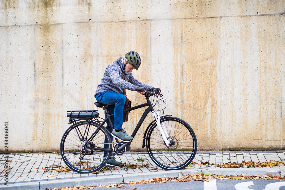 Naklejka premium Active senior man with electrobike standing outdoors in town.